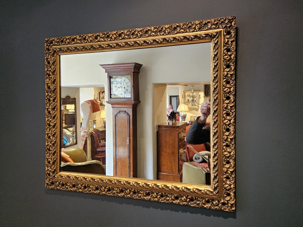 A large rectangular Victorian gilt mirror featuring a heavily carved timber frame with a gold leaf finish. View VI