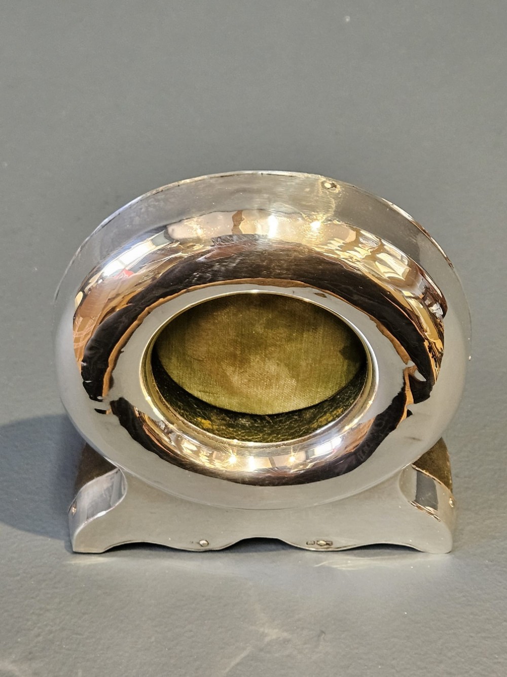 A circular sterling silver pocket watch holder with Chester hallmarks, featuring a recessed green velvet interior bezel and a shaped base. View VI
