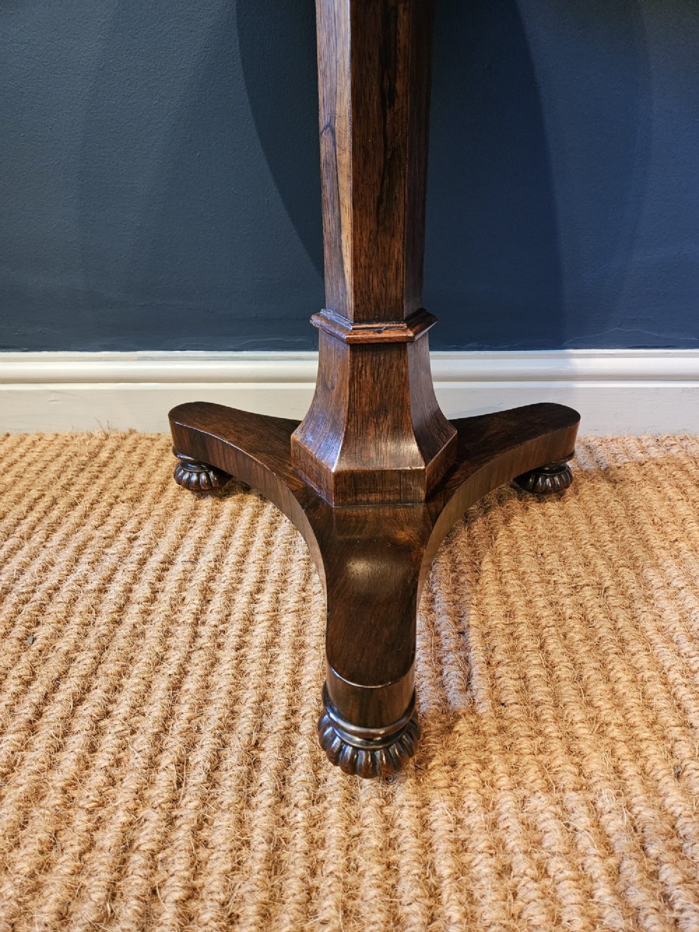 A round antique Regency rosewood occasional table featuring a rich grain, a central faceted pedestal column, and a tri-form platform base resting on carved feet. View III