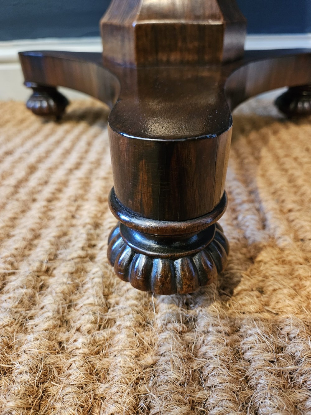 A round antique Regency rosewood occasional table featuring a rich grain, a central faceted pedestal column, and a tri-form platform base resting on carved feet. View IV