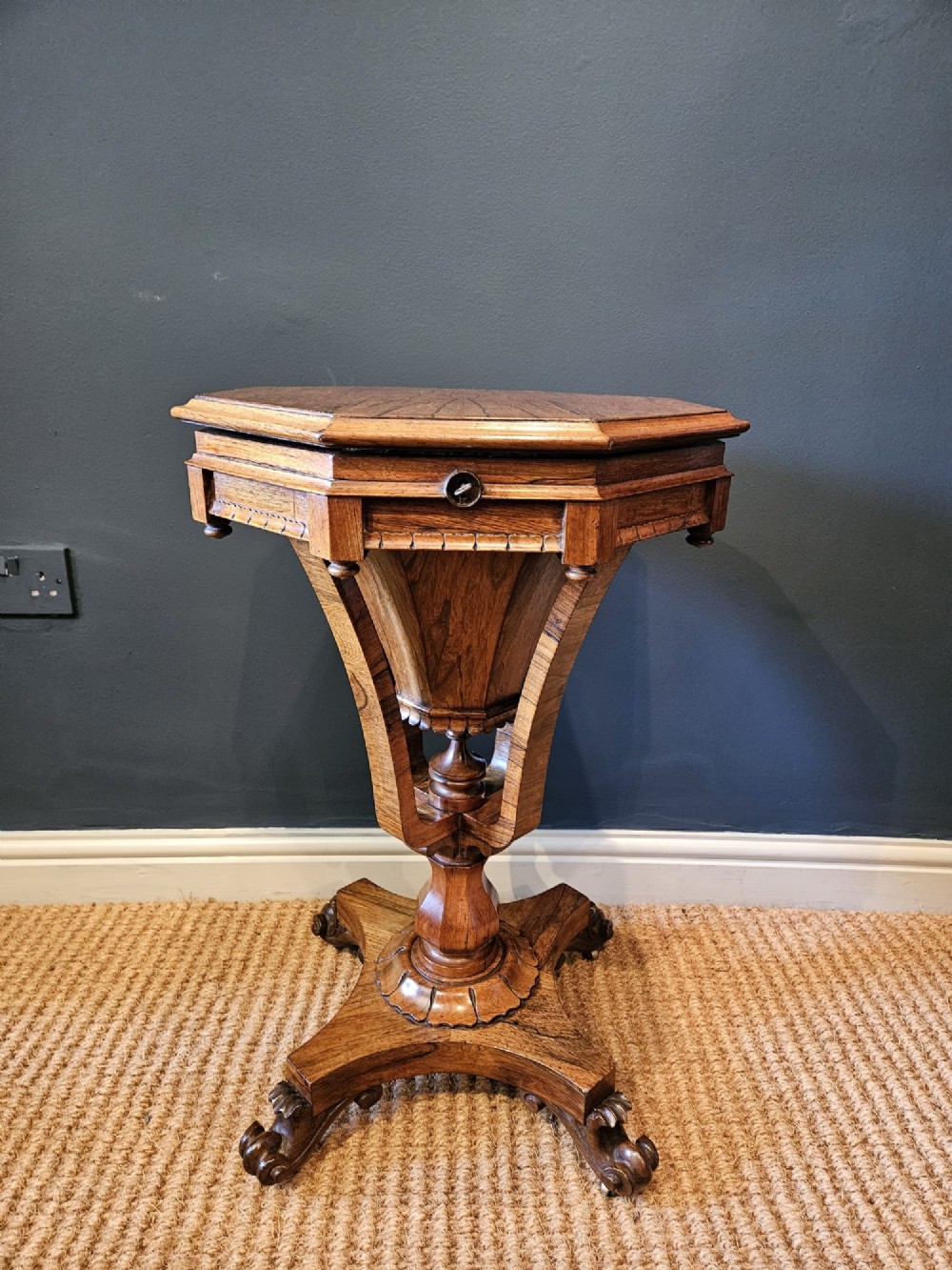 A William IV rosewood octagonal sewing work table featuring a tapered trumpet column supported by a carved quadform base with scroll feet.