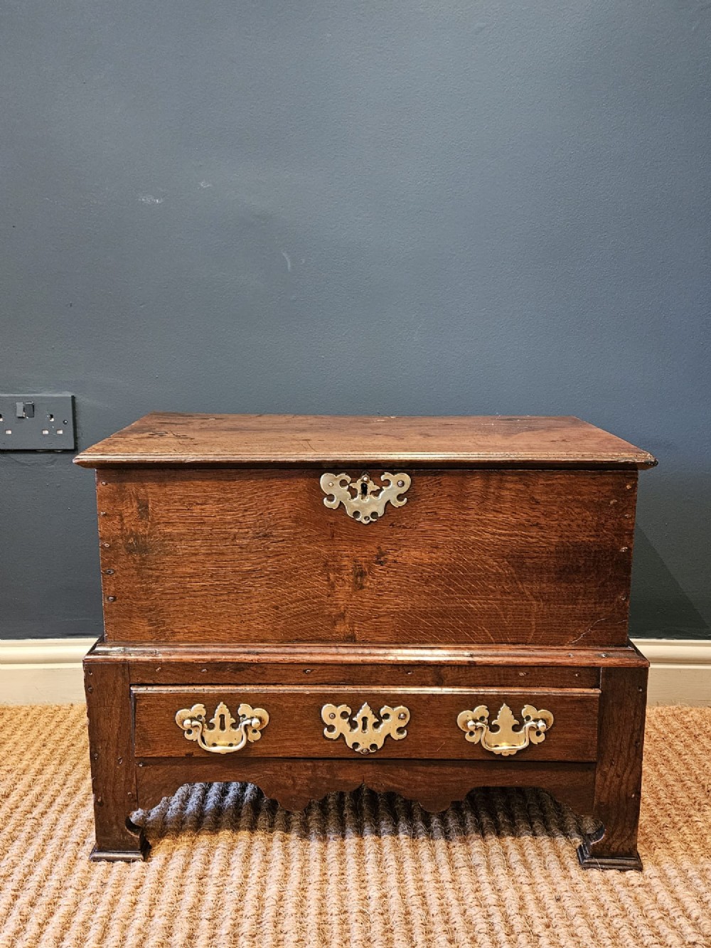 An antique 18th-century George II Welsh oak coffer bach with a hinged top lid, lower drawer, shaped apron, and brass escutcheons. View II