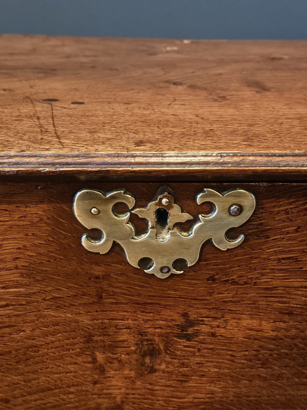 An antique 18th-century George II Welsh oak coffer bach with a hinged top lid, lower drawer, shaped apron, and brass escutcheons. View VI