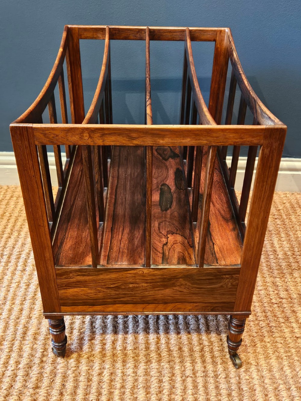 An antique Regency rosewood music canterbury featuring four slatted divisions with concave top rails, a single base drawer with turned wooden knobs, and turned legs on brass castors. View III