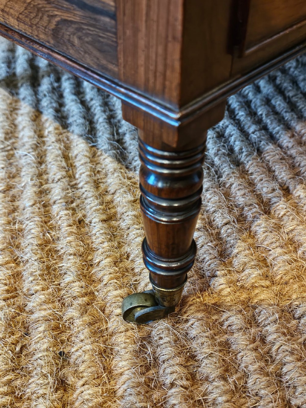 An antique Regency rosewood music canterbury featuring four slatted divisions with concave top rails, a single base drawer with turned wooden knobs, and turned legs on brass castors. View IV
