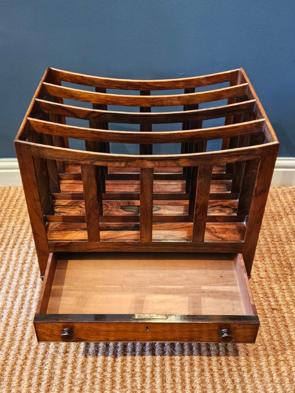 An antique Regency rosewood music canterbury featuring four slatted divisions with concave top rails, a single base drawer with turned wooden knobs, and turned legs on brass castors. View V