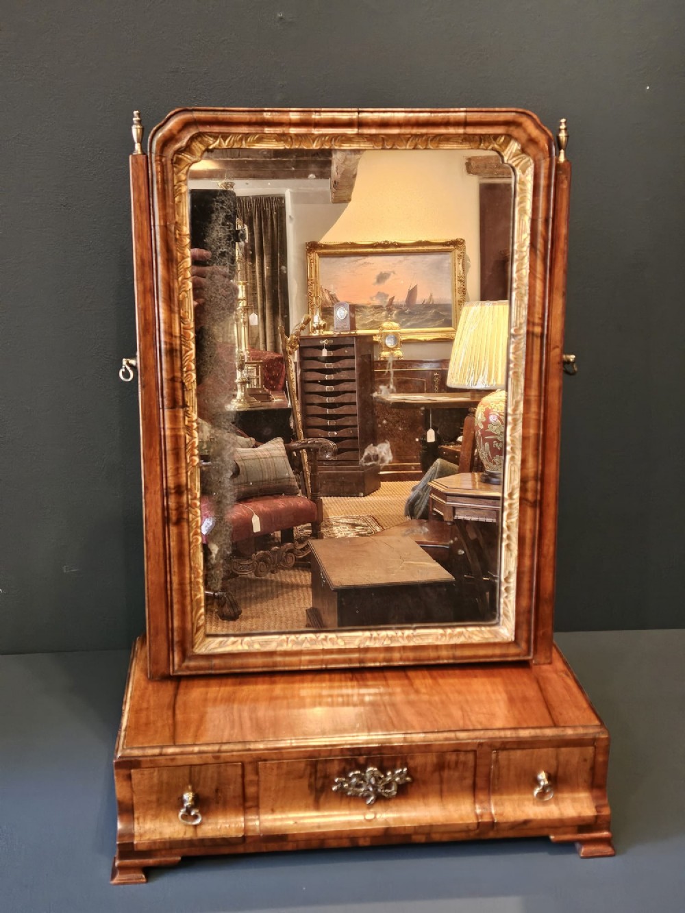 An 18th-century George II figured walnut toilet mirror featuring an adjustable frame with a gilded inner slip moulding above a single-drawer wooden base.