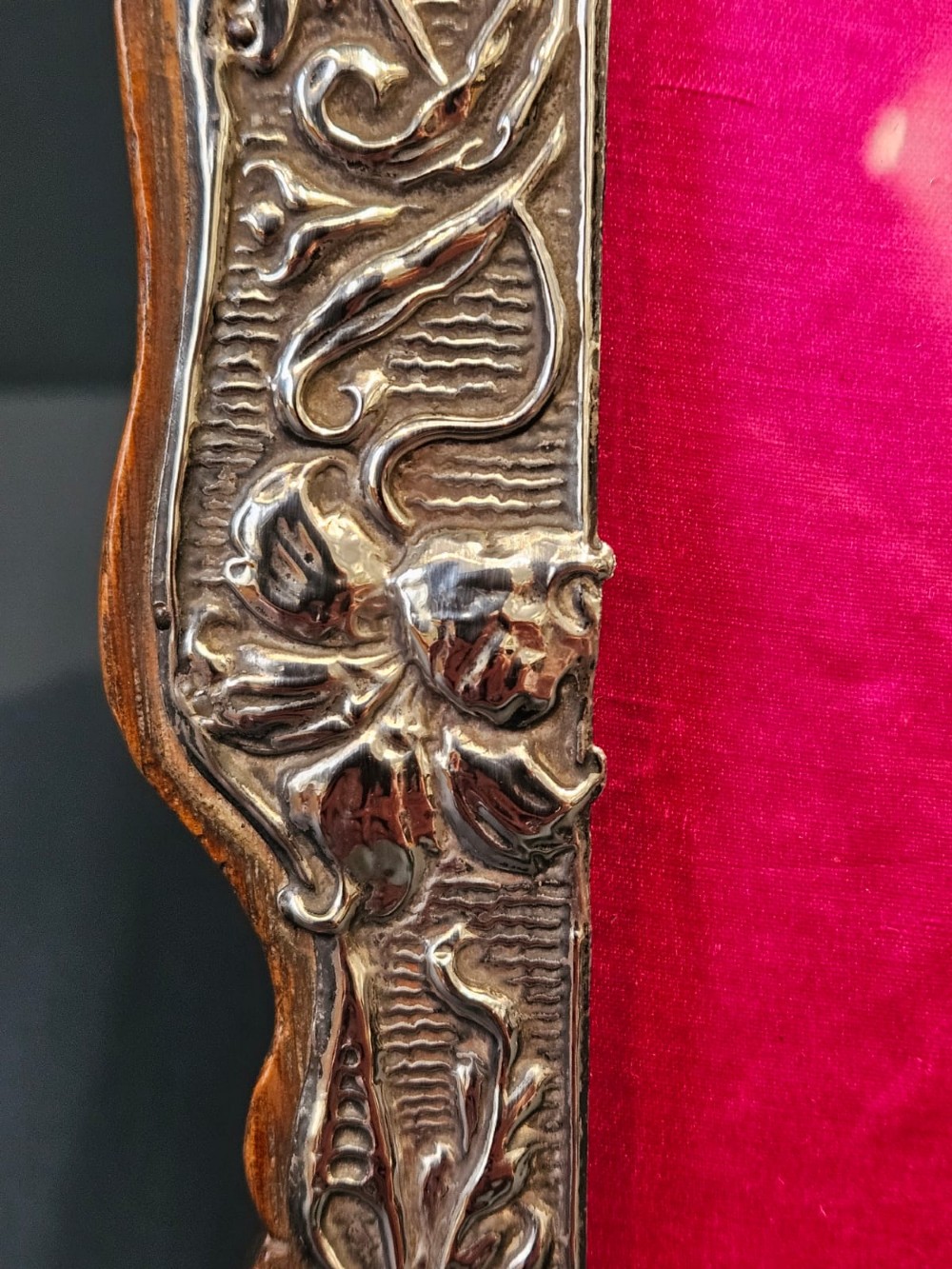 An Edwardian Art Nouveau silver photo frame featuring embossed floral scrollwork mounted on a shaped wooden backing with a bright pink interior insert. View IV