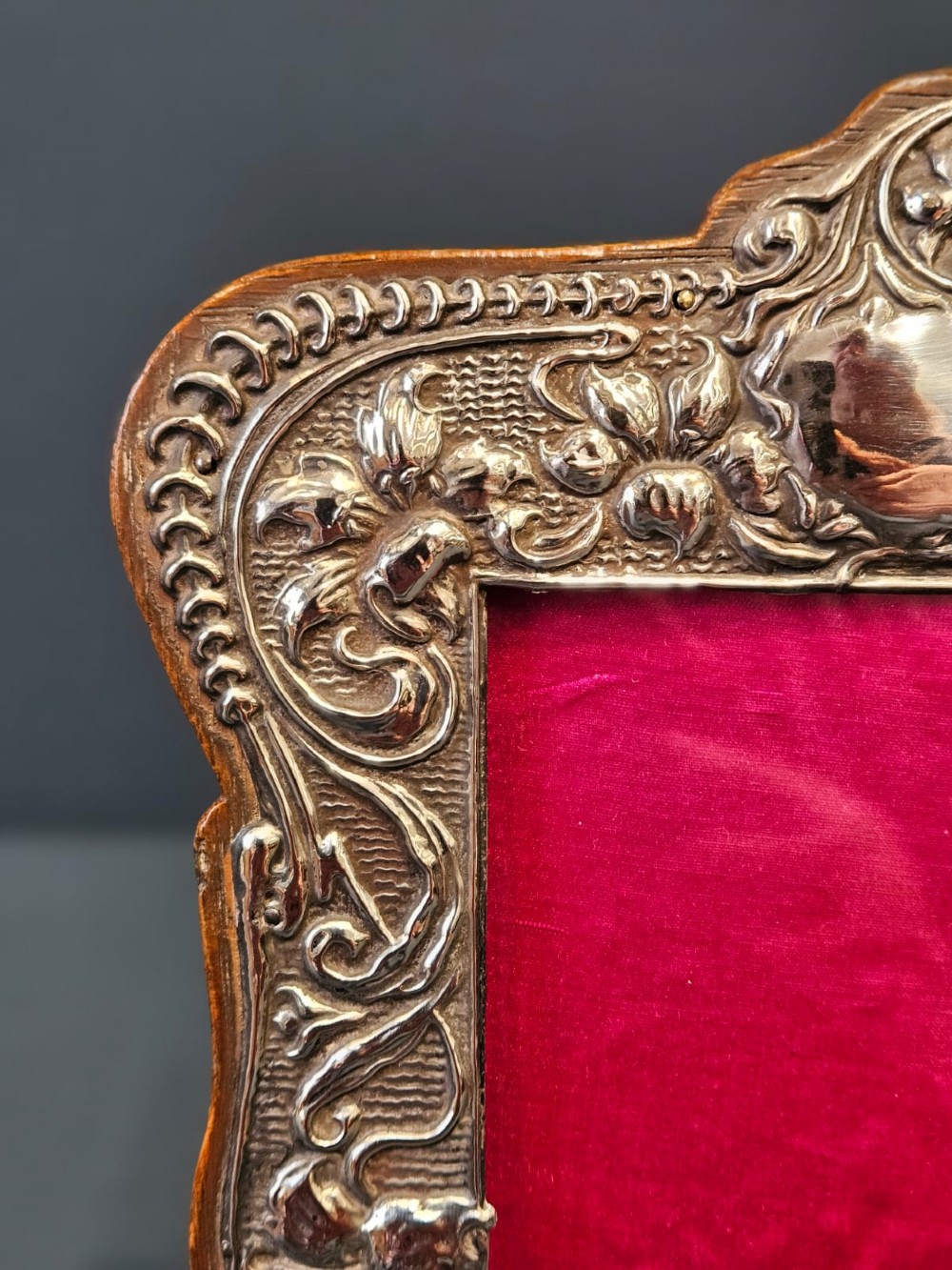 An Edwardian Art Nouveau silver photo frame featuring embossed floral scrollwork mounted on a shaped wooden backing with a bright pink interior insert. View VII