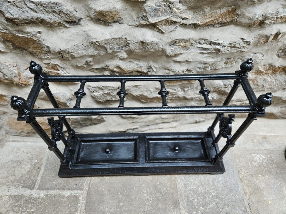 A black cast iron Victorian stick stand featuring finial top ornamentation, side supports, and two removable drip trays at the base. View II