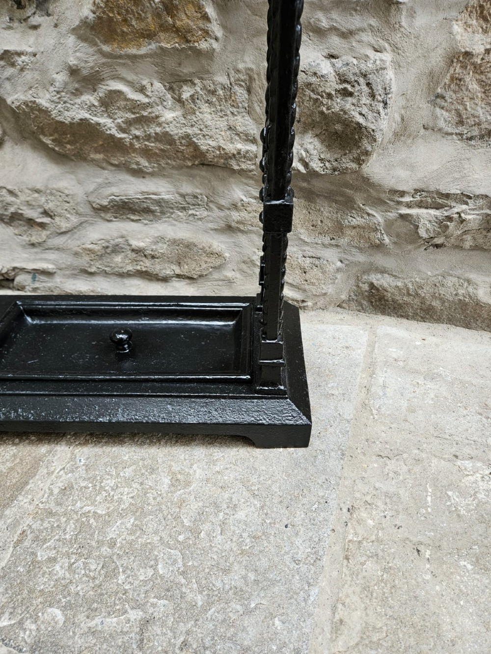 A black cast iron Victorian stick stand featuring finial top ornamentation, side supports, and two removable drip trays at the base. View VIII