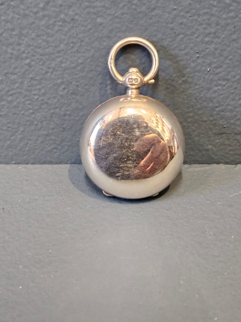 A circular polished sterling silver sovereign case with a top suspension ring and hallmarked stem.