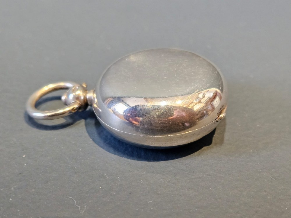 A circular polished sterling silver sovereign case with a top suspension ring and hallmarked stem. View II