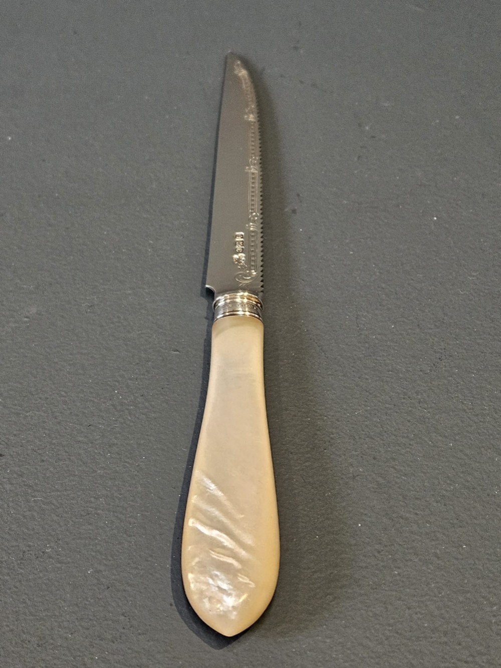 A hallmarked silver fruit serving knife with an engraved blade and mother-of-pearl handle presented inside an open dark velvet-lined case. View V