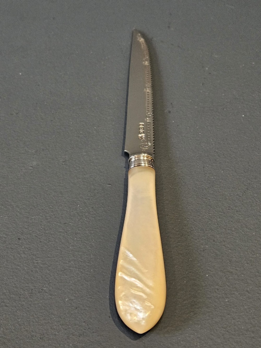 A hallmarked silver fruit serving knife with an engraved blade and mother-of-pearl handle presented inside an open dark velvet-lined case. View VII