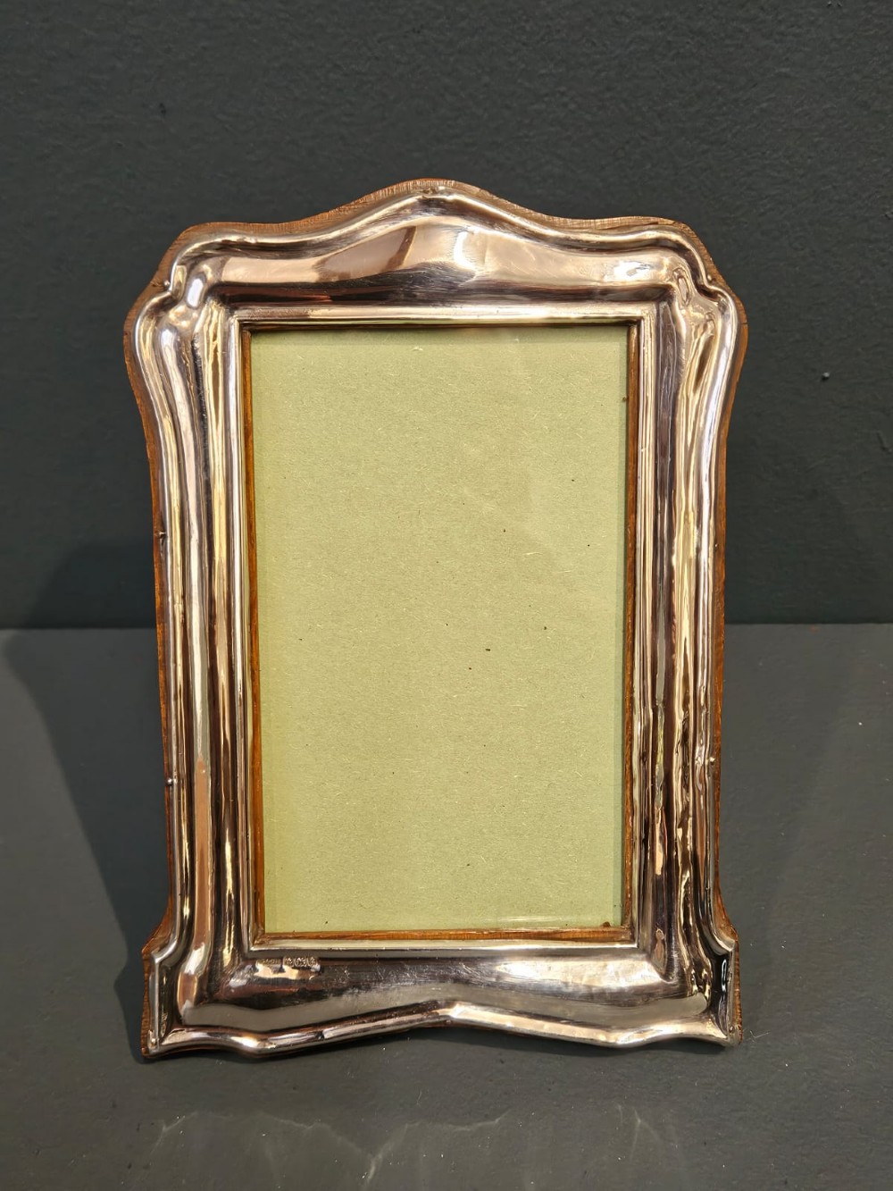 A freestanding rectangular silver photo frame featuring a shaped rim, embossed border, and a wooden back.