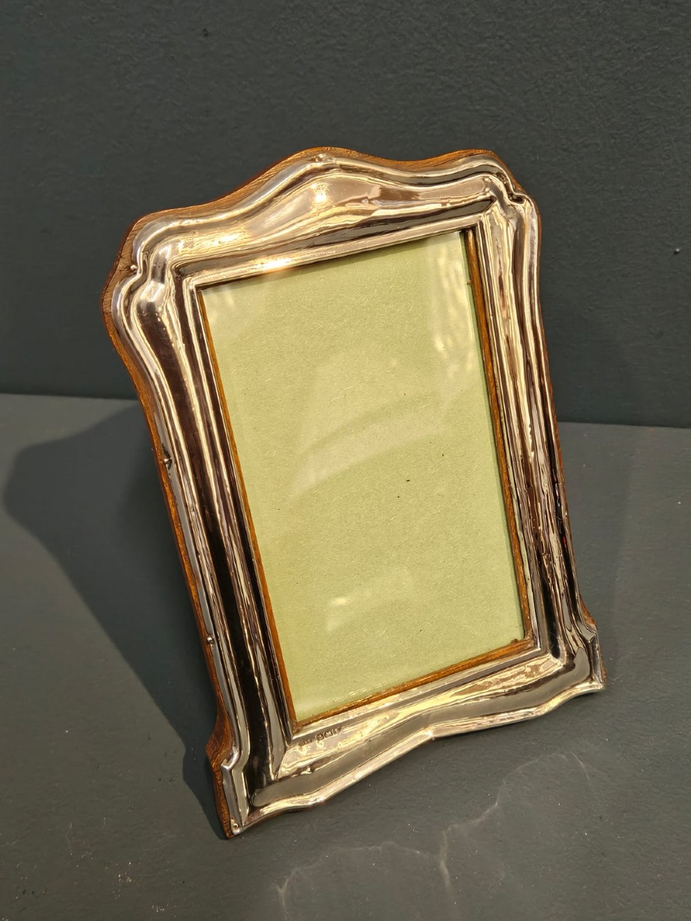 A freestanding rectangular silver photo frame featuring a shaped rim, embossed border, and a wooden back. View II