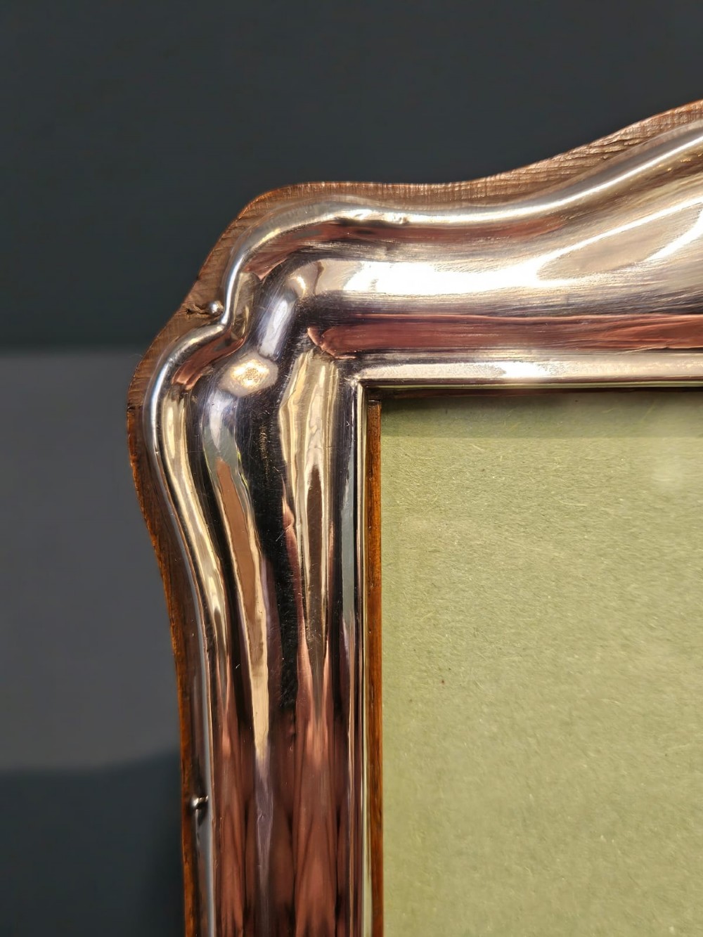 A freestanding rectangular silver photo frame featuring a shaped rim, embossed border, and a wooden back. View III