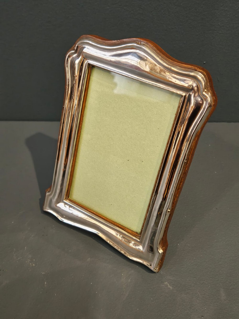 A freestanding rectangular silver photo frame featuring a shaped rim, embossed border, and a wooden back. View IV