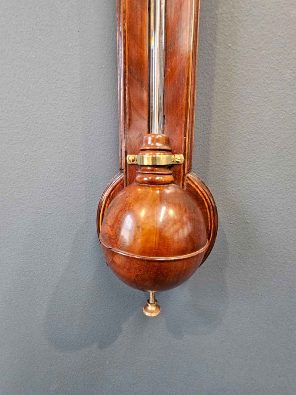 A wall-mounted Georgian mahogany stick barometer featuring a capillary glass tube, engraved silvered register plate, and a rounded wooden cistern cover at the base. View V
