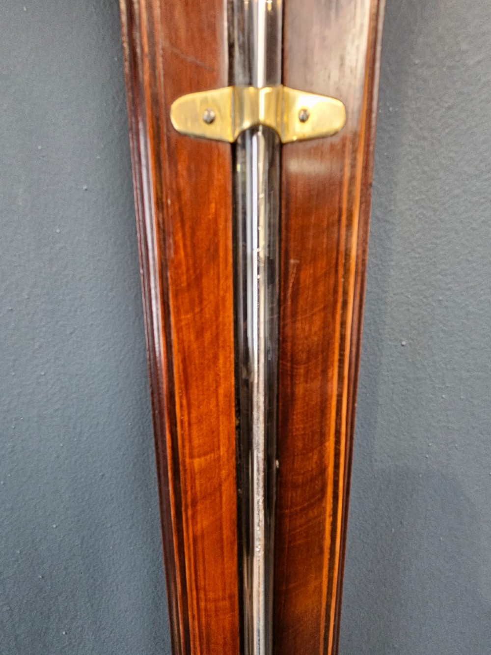 A wall-mounted Georgian mahogany stick barometer featuring a capillary glass tube, engraved silvered register plate, and a rounded wooden cistern cover at the base. View VI