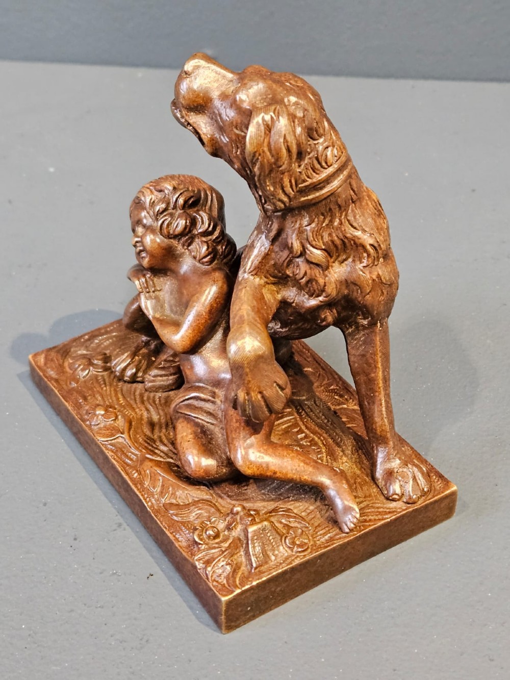 An Edwardian bronze sculpture depicting a sleeping child resting beside an alert dog on a rectangular relief base. View II