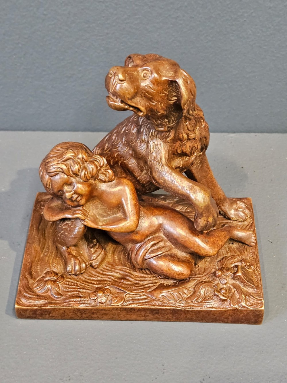An Edwardian bronze sculpture depicting a sleeping child resting beside an alert dog on a rectangular relief base. View IV