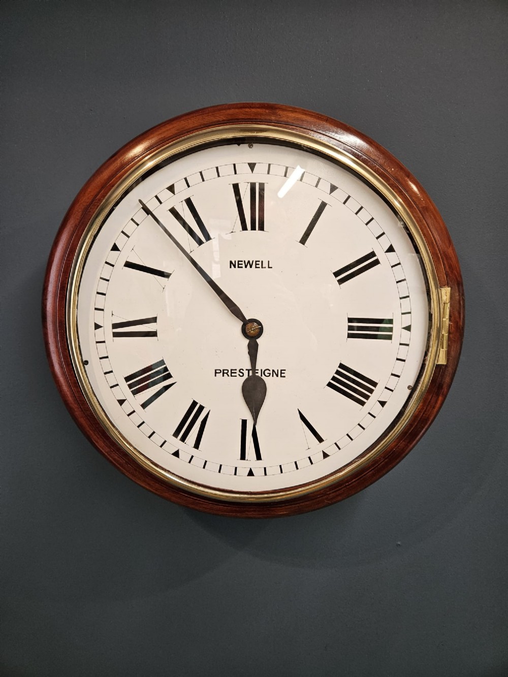 A circular Victorian wall clock featuring a mahogany wooden frame, a white dial with black Roman numerals, spade hands, and a brass bezel.