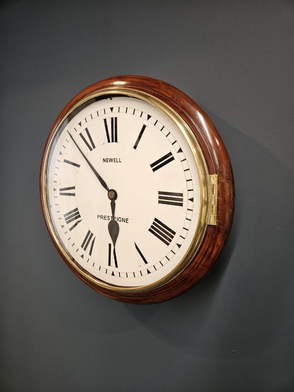 A circular Victorian wall clock featuring a mahogany wooden frame, a white dial with black Roman numerals, spade hands, and a brass bezel. View II