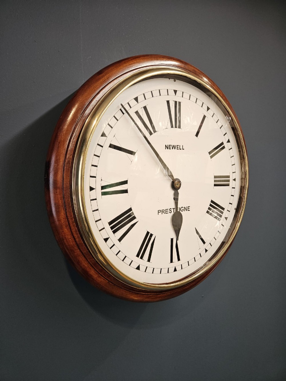 A circular Victorian wall clock featuring a mahogany wooden frame, a white dial with black Roman numerals, spade hands, and a brass bezel. View IV