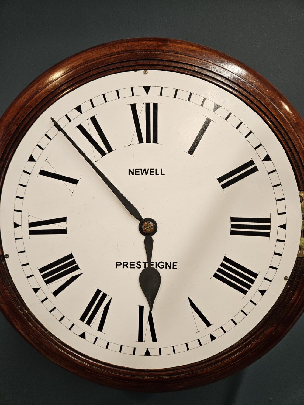A circular Victorian wall clock featuring a mahogany wooden frame, a white dial with black Roman numerals, spade hands, and a brass bezel. View VI