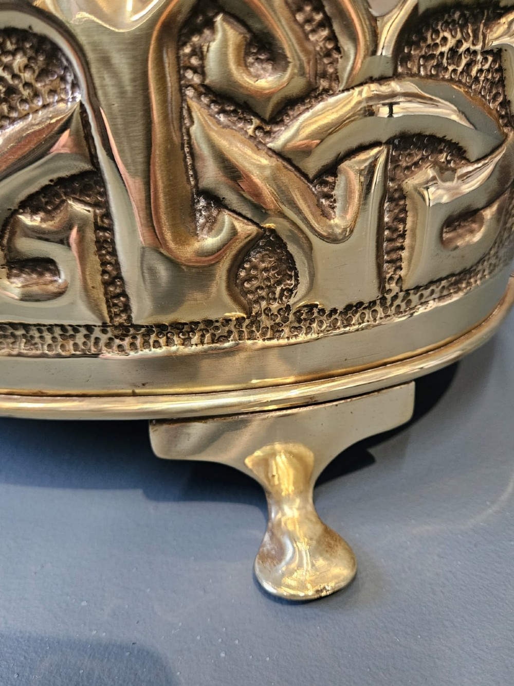 An oval polished brass planter featuring embossed Glasgow School Celtic knotwork on a stippled background, raised on short bracket feet with side handles. View IV