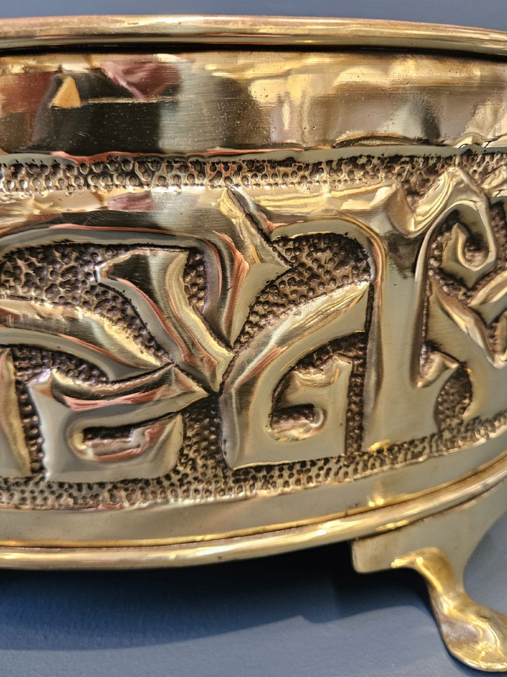 An oval polished brass planter featuring embossed Glasgow School Celtic knotwork on a stippled background, raised on short bracket feet with side handles. View VI