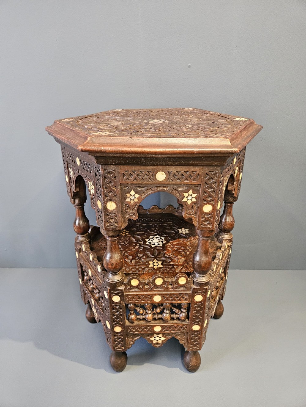 An octagonal dark wood Moorish table featuring carved geometric lattice panels, horseshoe arches, and inlaid bone star motifs.