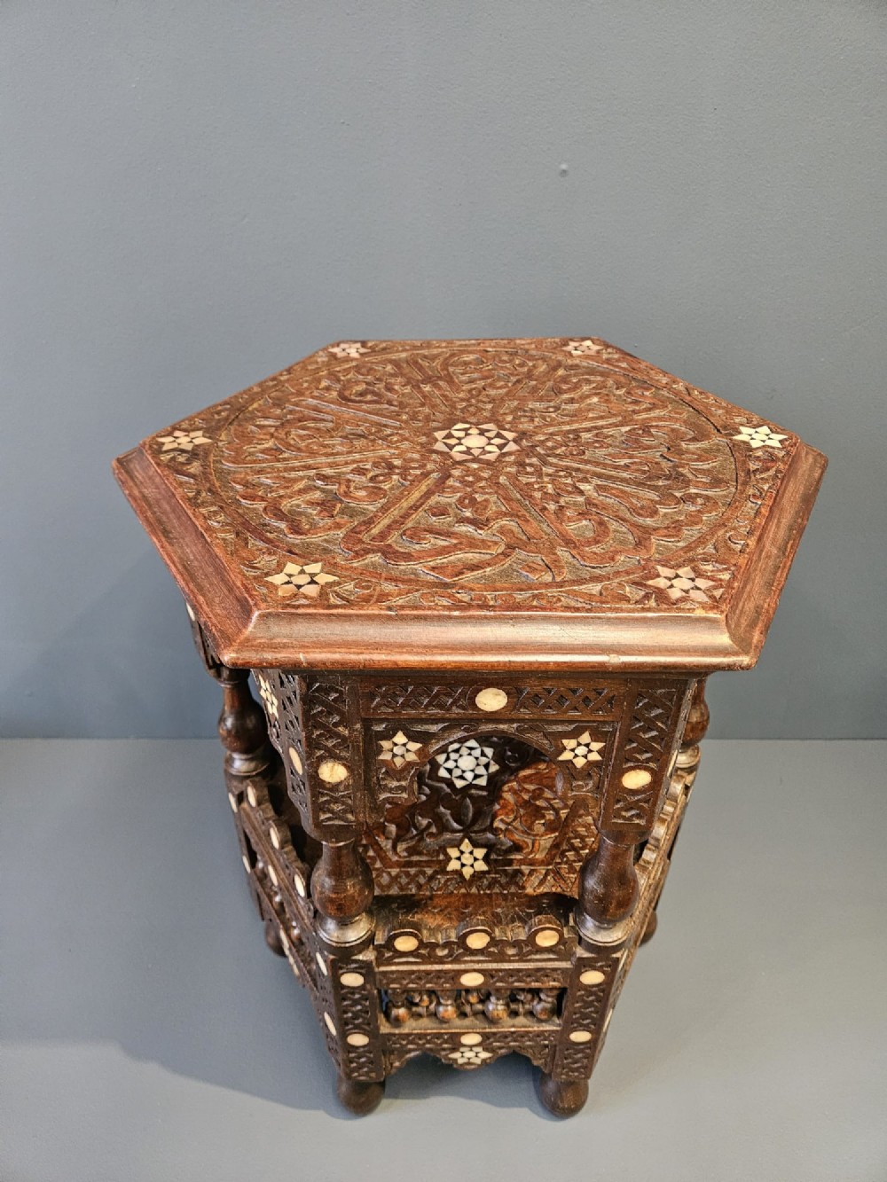 An octagonal dark wood Moorish table featuring carved geometric lattice panels, horseshoe arches, and inlaid bone star motifs. View V