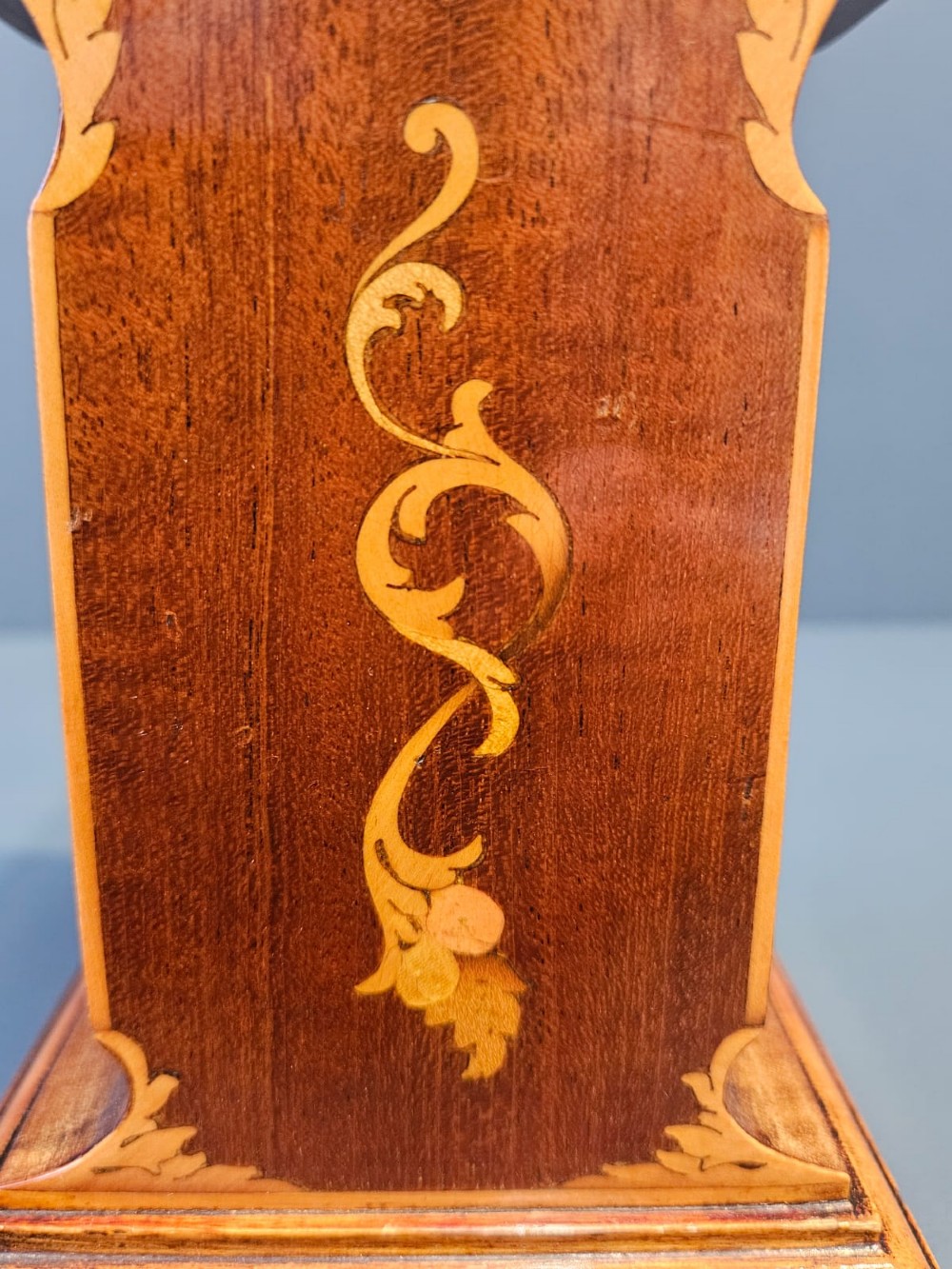 An Edwardian waisted mahogany mantel clock featuring light wood marquetry inlay, a glazed brass bezel, and Roman numerals on a white dial. View III