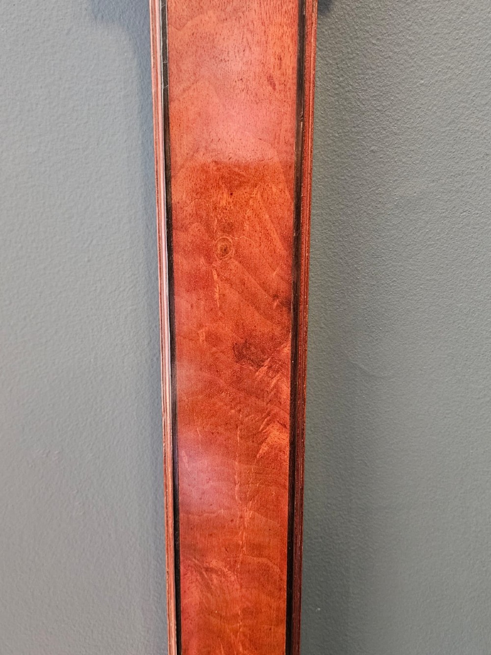 A slim vertical Georgian mahogany stick barometer featuring a broken-arch pediment with a brass finial, an engraved silvered register plate, and a turned cistern cover at the base. View II