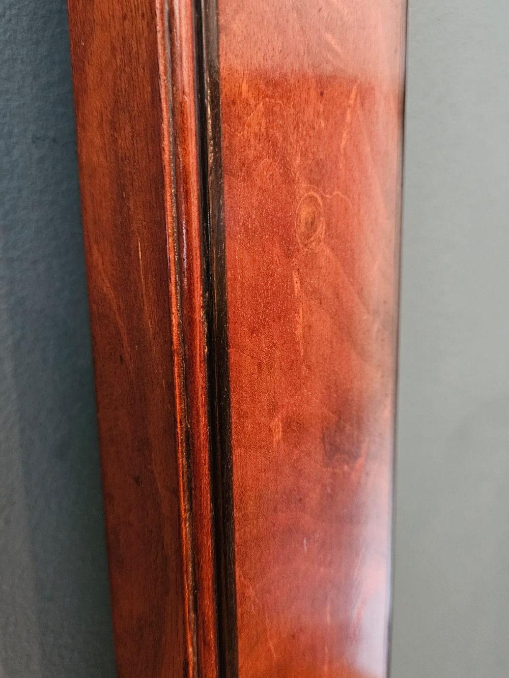 A slim vertical Georgian mahogany stick barometer featuring a broken-arch pediment with a brass finial, an engraved silvered register plate, and a turned cistern cover at the base. View V