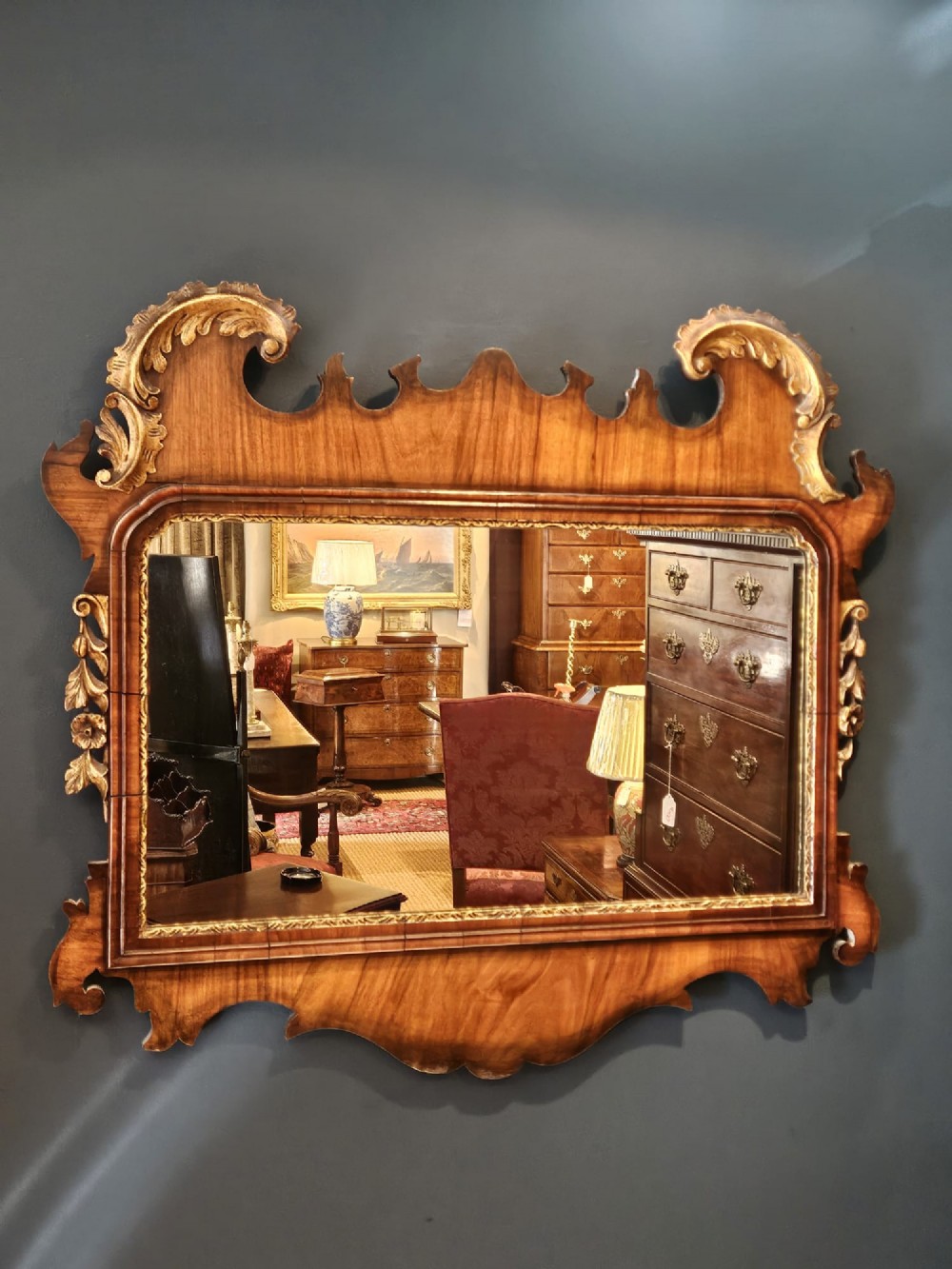 A horizontal George III style landscape wall mirror featuring a shaped mahogany frame accented with carved parcel-gilt leaf scrollwork.