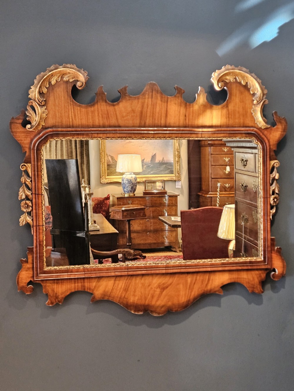 A horizontal George III style landscape wall mirror featuring a shaped mahogany frame accented with carved parcel-gilt leaf scrollwork. View II