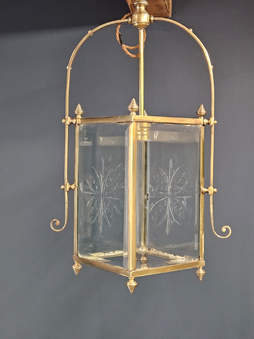 An Edwardian brass-framed hall lantern featuring clear glass panels with cut starburst patterns, finial accents, and an arched hanging harness.