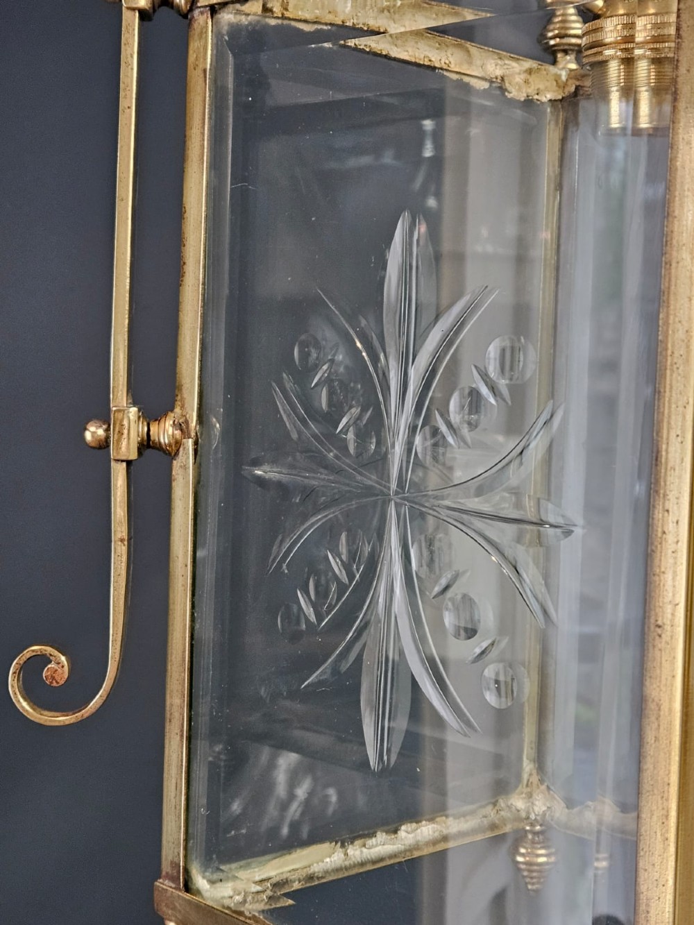 An Edwardian brass-framed hall lantern featuring clear glass panels with cut starburst patterns, finial accents, and an arched hanging harness. View III