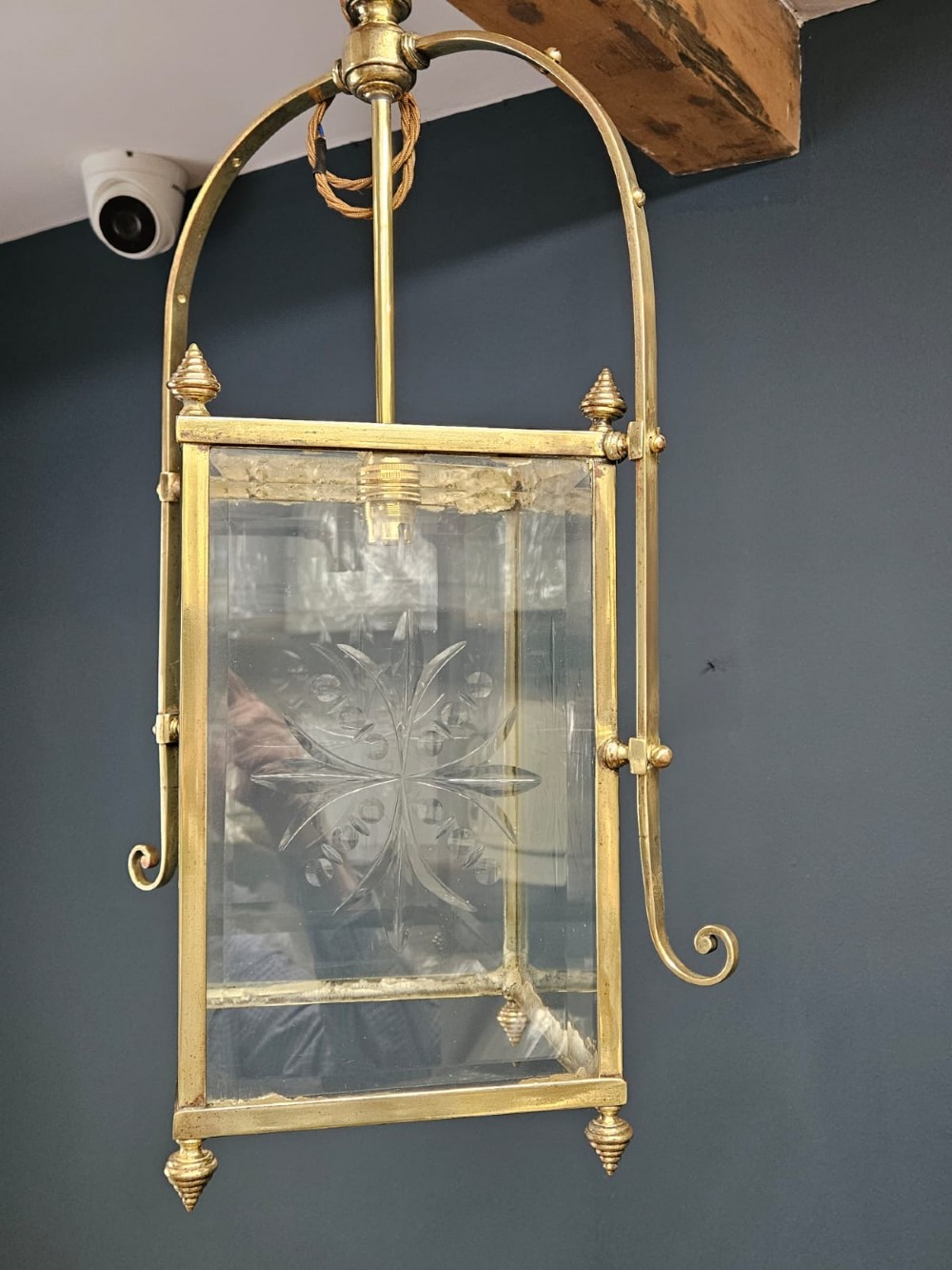 An Edwardian brass-framed hall lantern featuring clear glass panels with cut starburst patterns, finial accents, and an arched hanging harness. View V