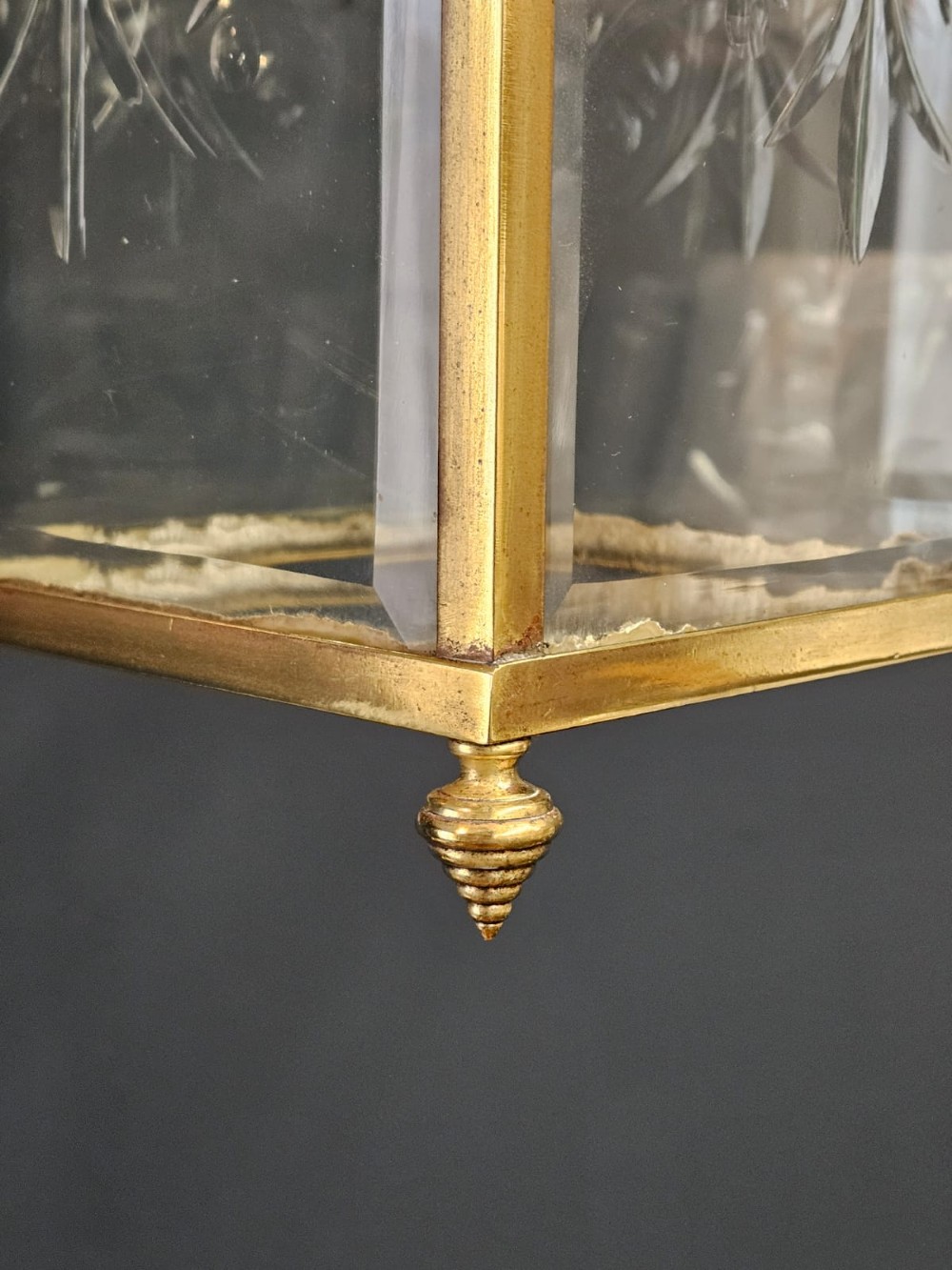 An Edwardian brass-framed hall lantern featuring clear glass panels with cut starburst patterns, finial accents, and an arched hanging harness. View VI