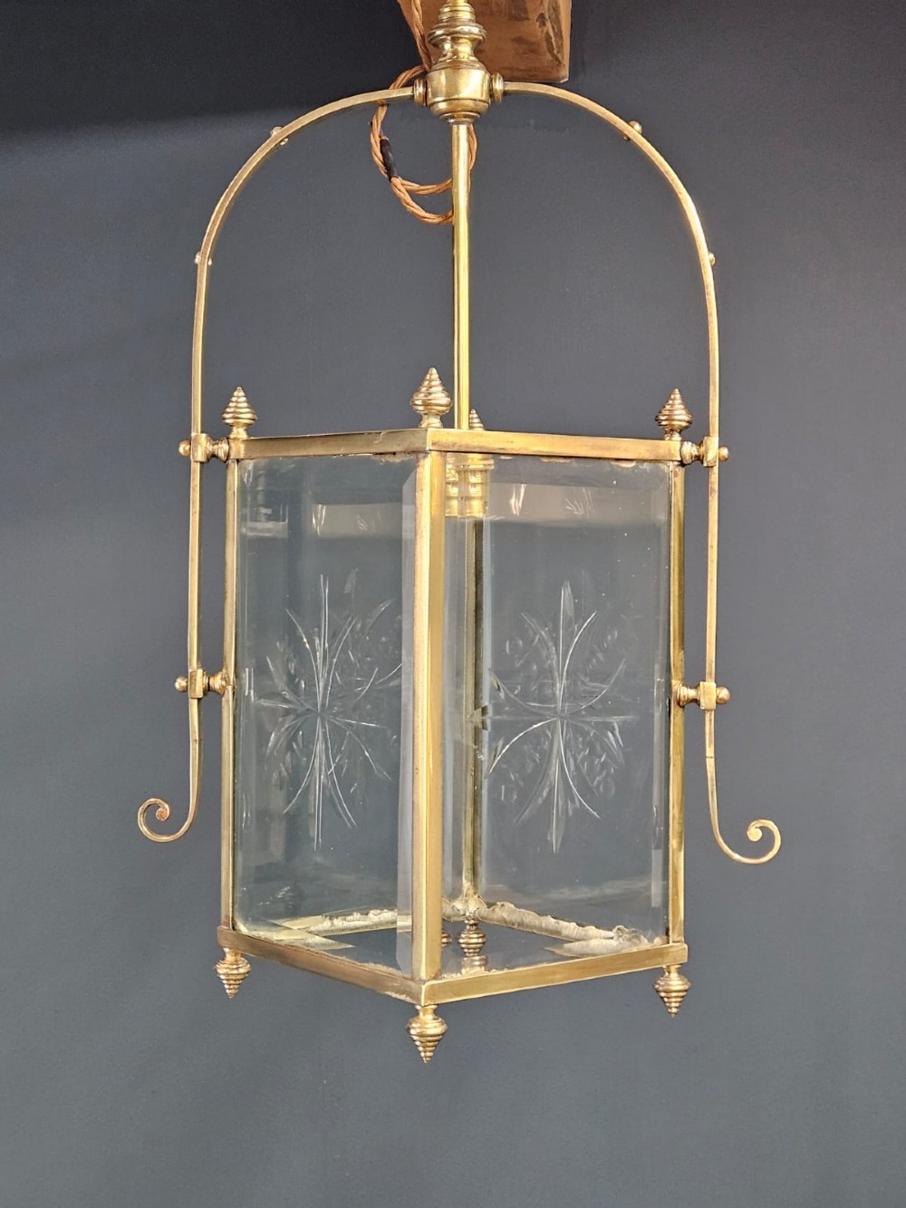 An Edwardian brass-framed hall lantern featuring clear glass panels with cut starburst patterns, finial accents, and an arched hanging harness. View VII