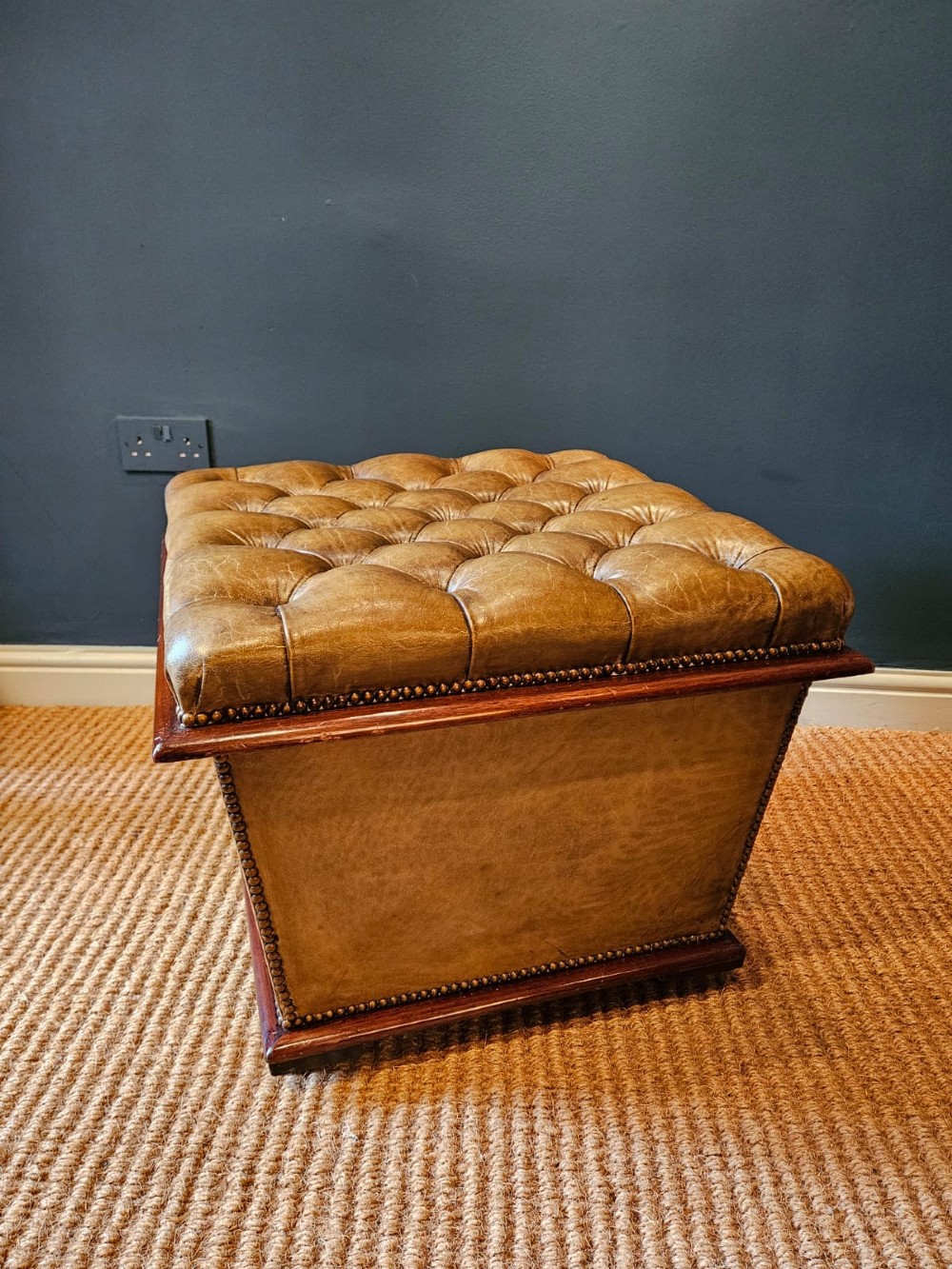 A deep-buttoned tan leather Victorian ottoman stool featuring brass stud trim and set upon a mahogany base with castors. View II