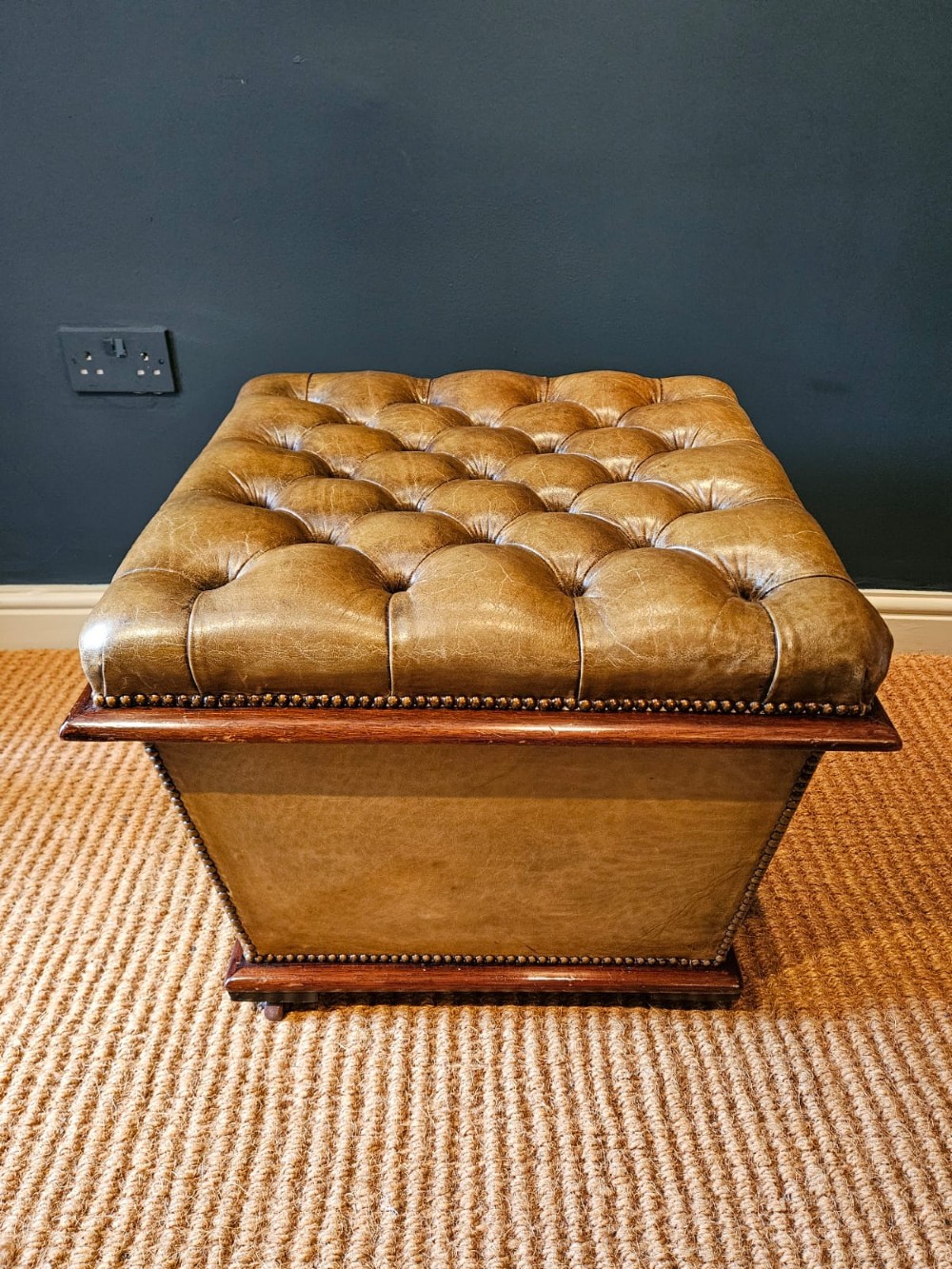 A deep-buttoned tan leather Victorian ottoman stool featuring brass stud trim and set upon a mahogany base with castors. View III