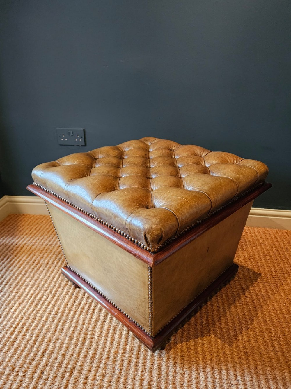A deep-buttoned tan leather Victorian ottoman stool featuring brass stud trim and set upon a mahogany base with castors. View IV
