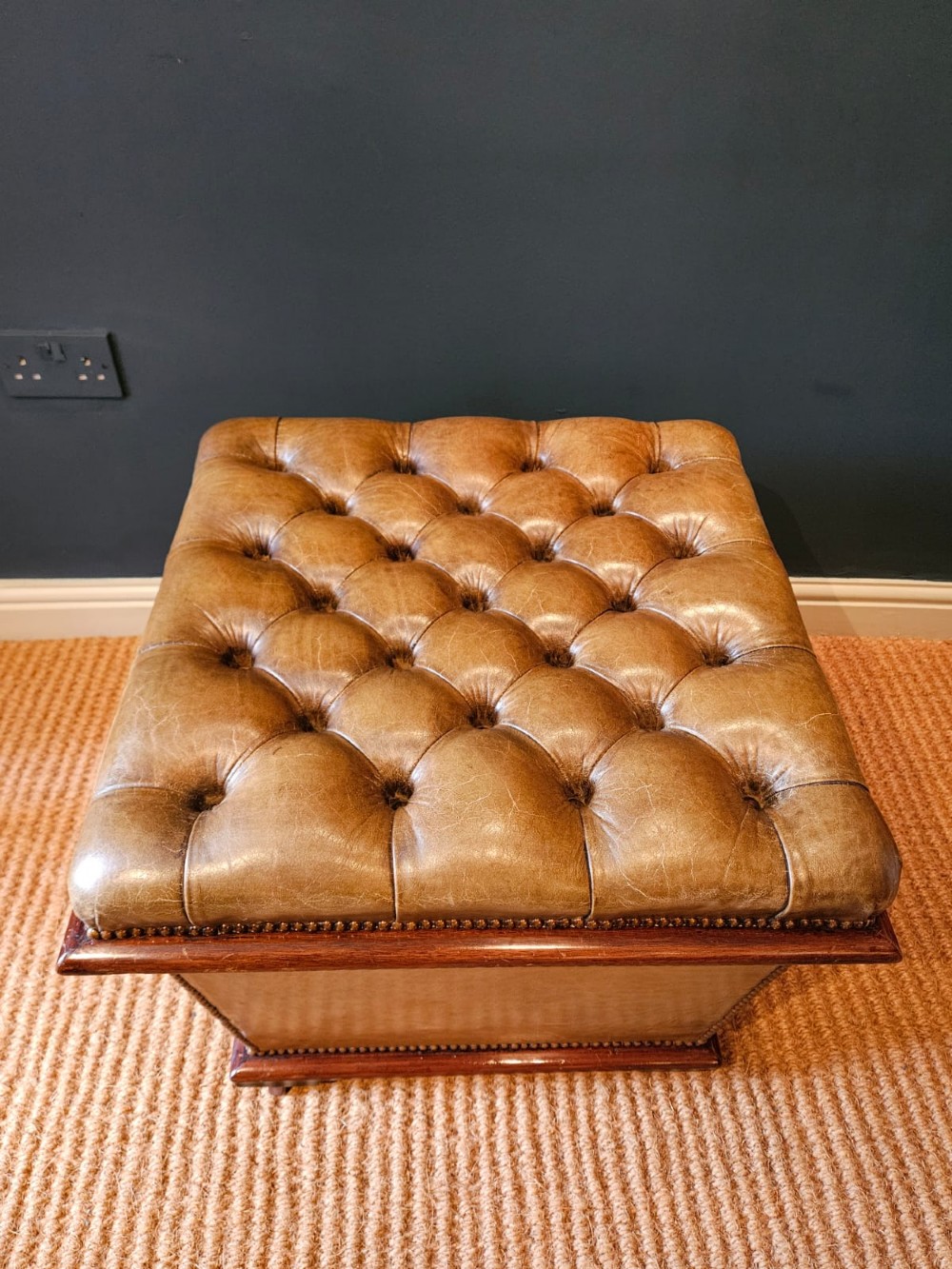 A deep-buttoned tan leather Victorian ottoman stool featuring brass stud trim and set upon a mahogany base with castors. View V