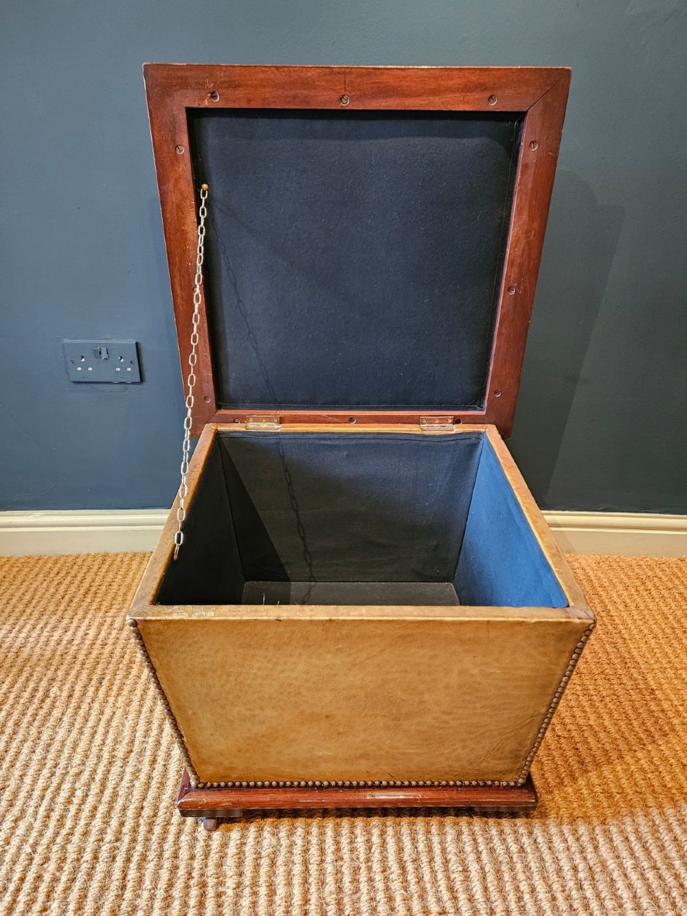 A deep-buttoned tan leather Victorian ottoman stool featuring brass stud trim and set upon a mahogany base with castors. View VII